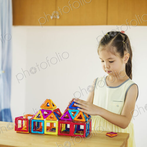 A girl playing, building a structure with colourful geometric shapes.