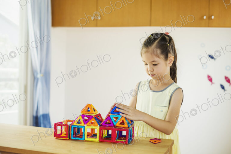 A girl playing, building a structure with colourful geometric shapes.