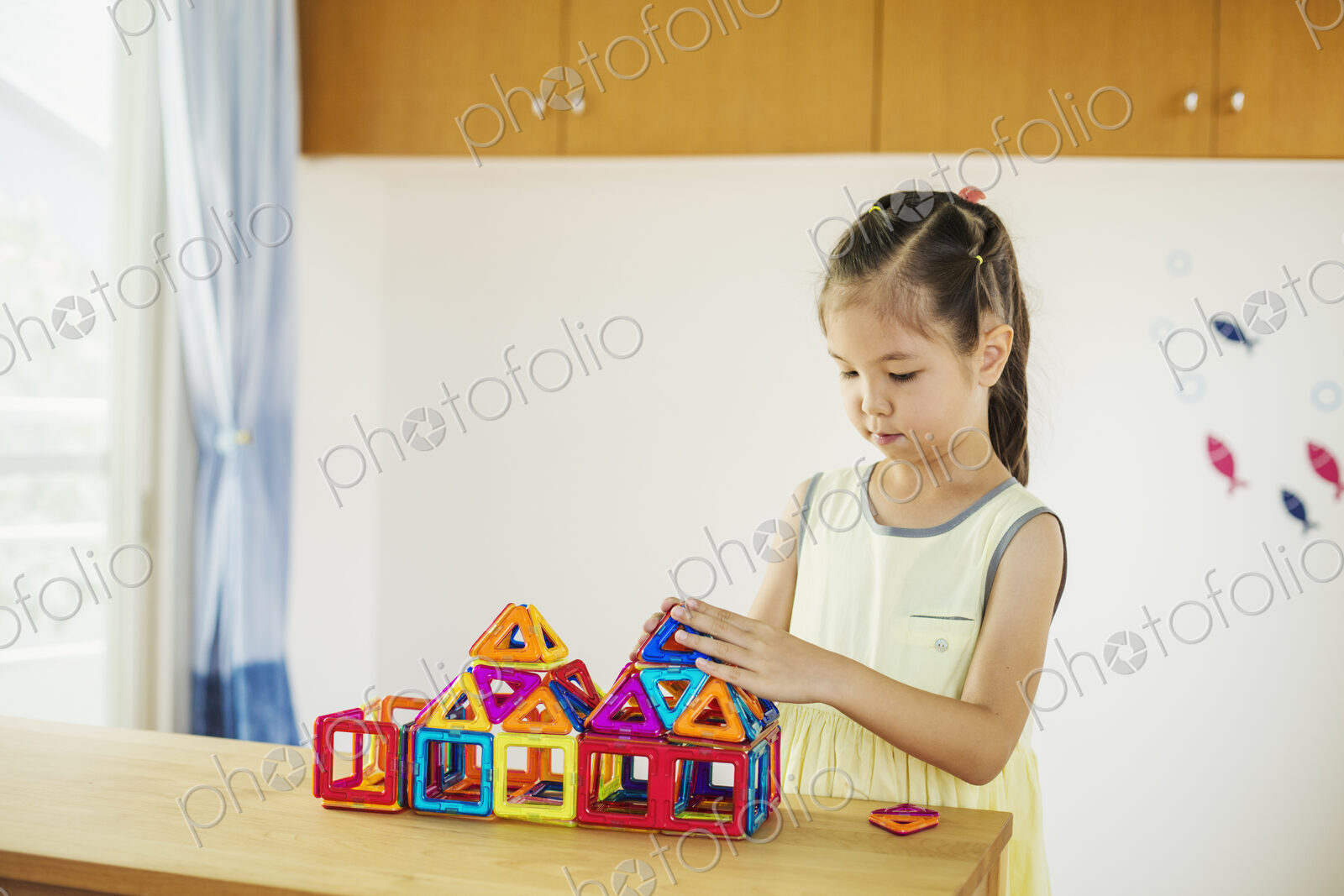 A girl playing, building a structure with colourful geometric shapes.