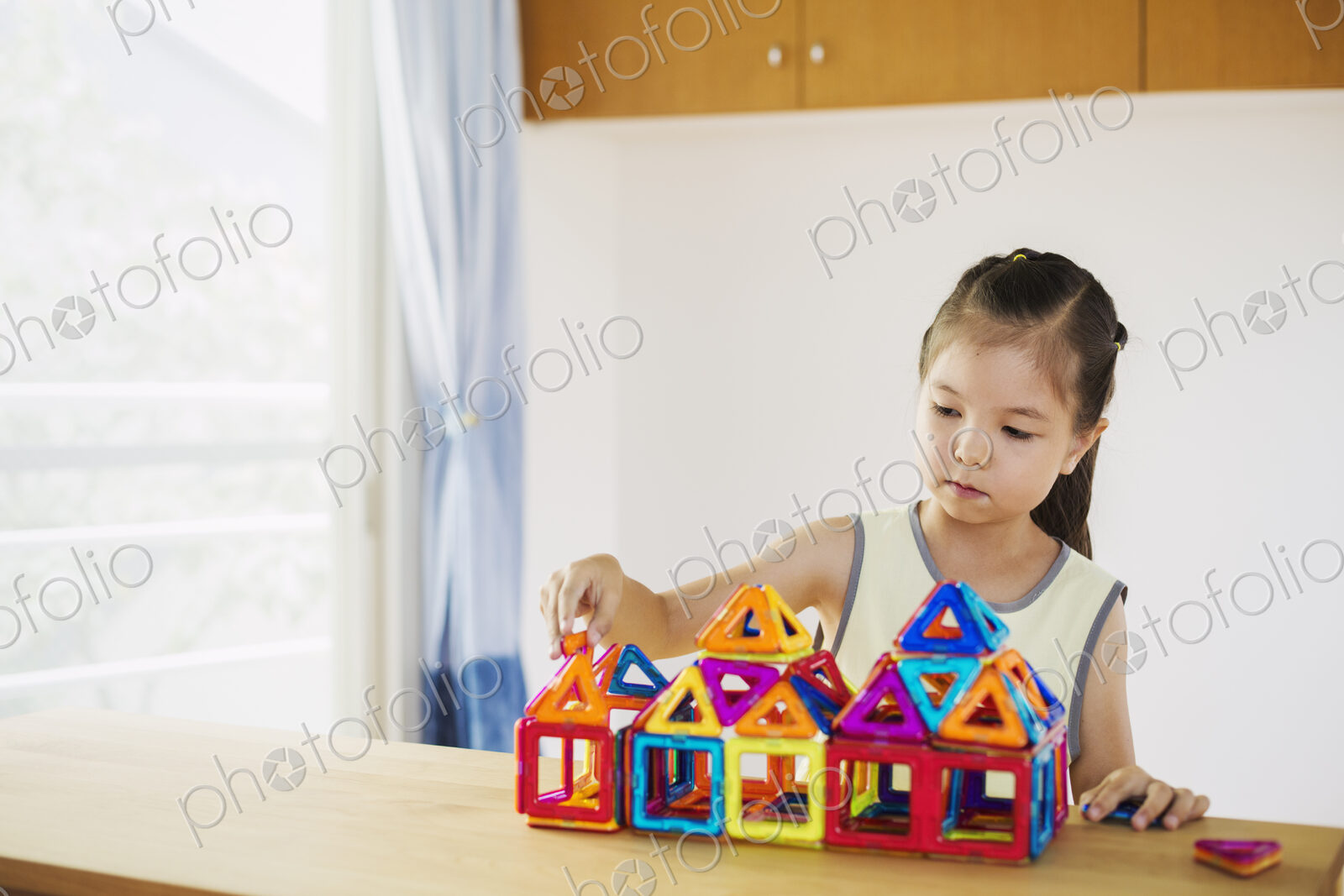 A girl playing, building a structure with colourful geometric shapes.
