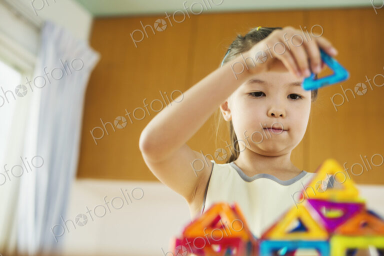 A girl playing, building a structure with colourful geometric shapes.