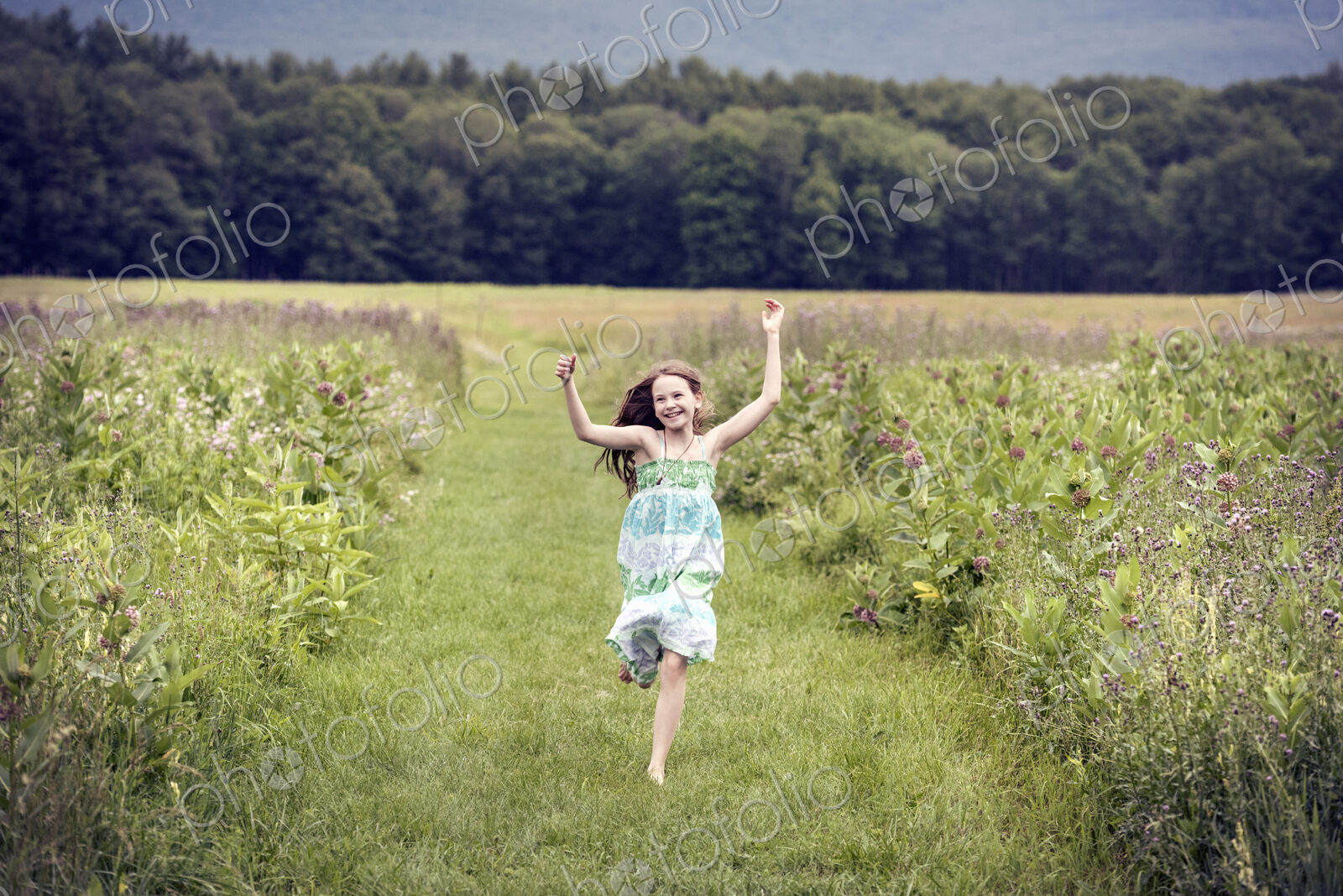 A girl running through a meadowwith her arms above her head.
