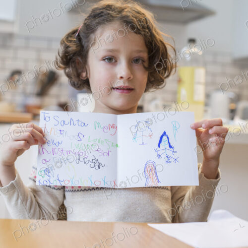 A girl showing her home made Christmas card, a letter to Santa Claus, with drawings… A girl showing her home made Christmas card, a letter to Santa Claus, with drawings…