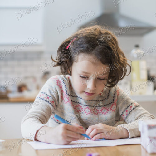 A girl sitting at a kitchen table writing a card or letter.