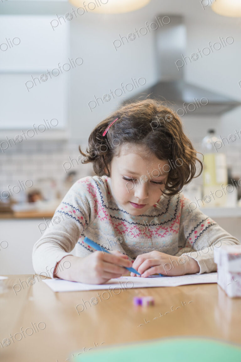 A girl sitting at a kitchen table writing a card or letter.