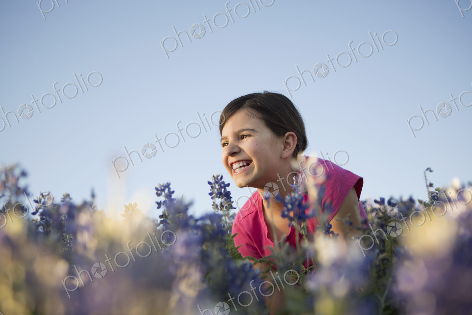 A girl sitting in a field of tall grass and blue wild flowers.