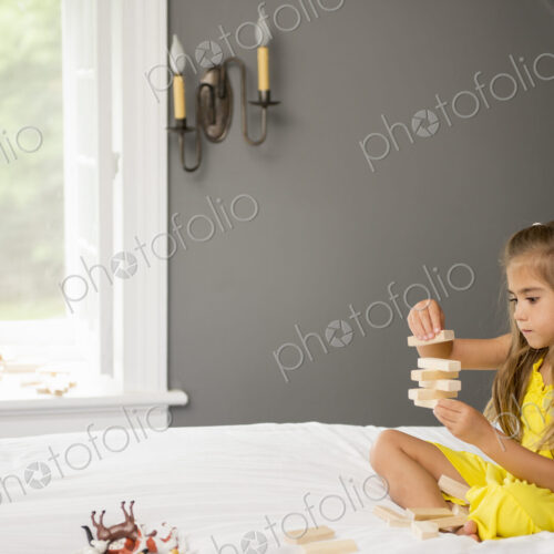 A girl sitting on a bed, playing with building blocks.