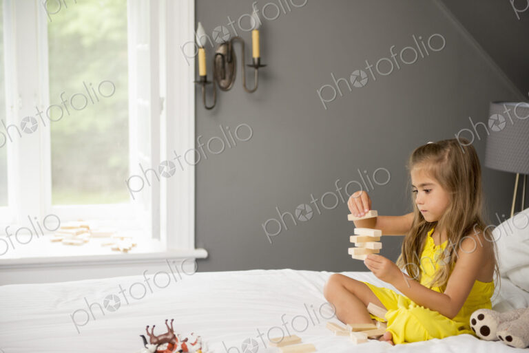 A girl sitting on a bed, playing with building blocks.