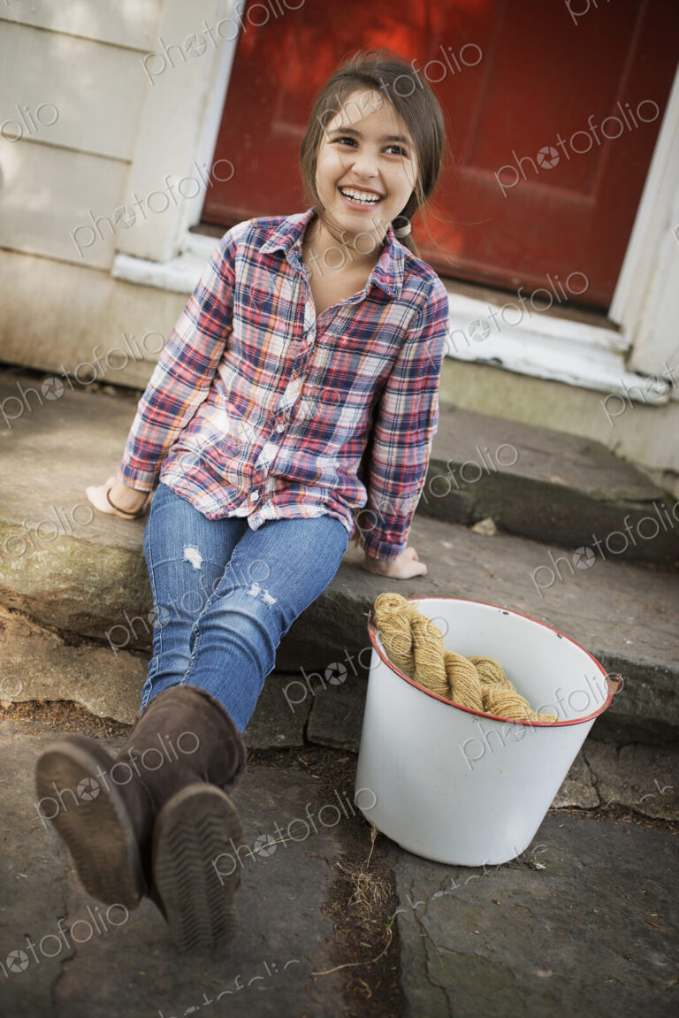 A girl sitting on a step, with a large iron pail and gloves.
