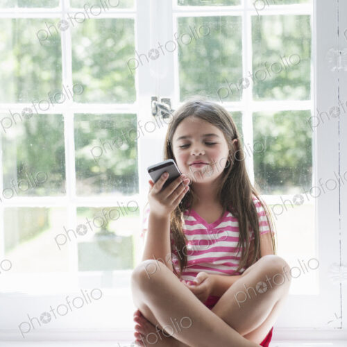 A girl sitting playing, holding a smart phone.