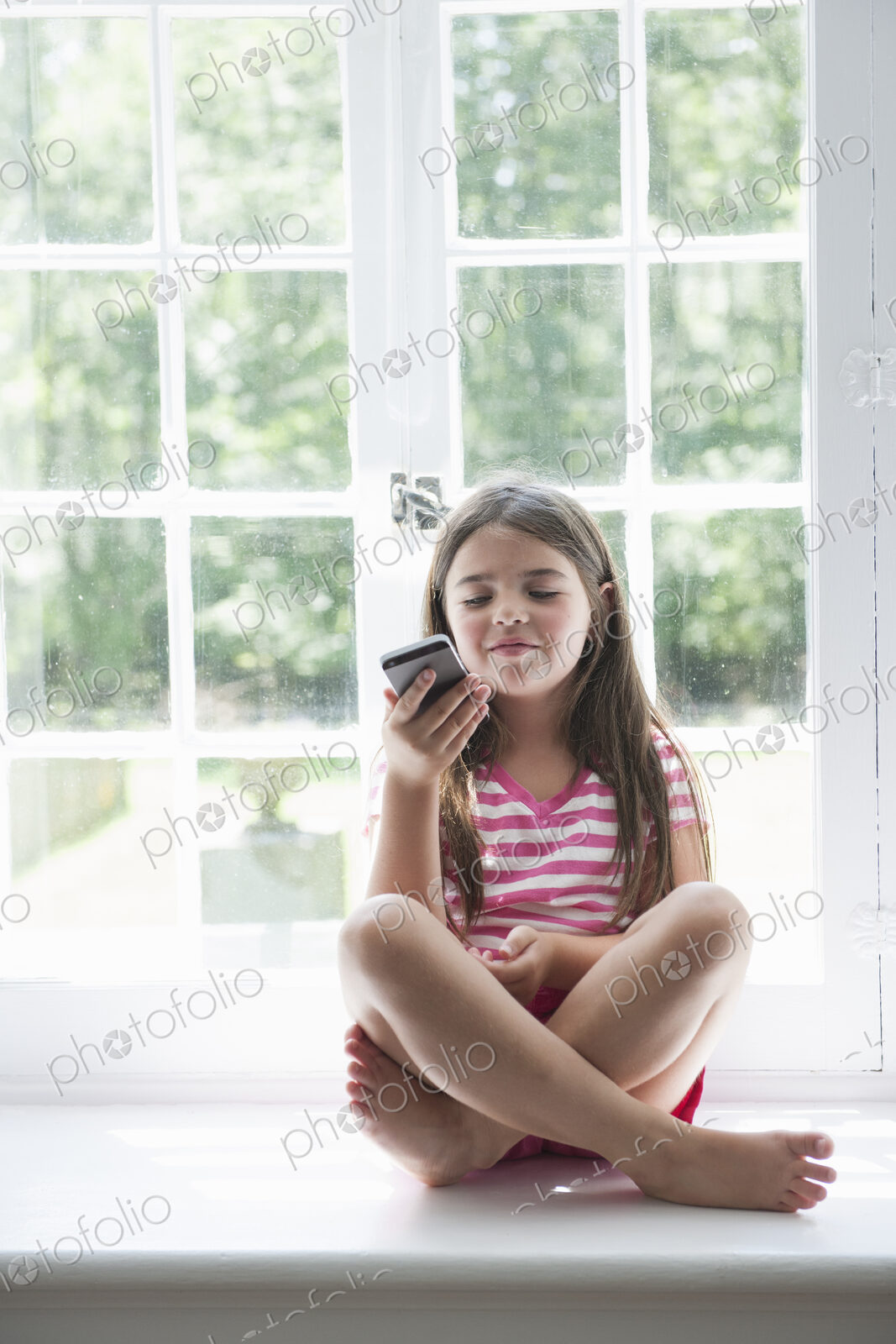 A girl sitting playing, holding a smart phone.