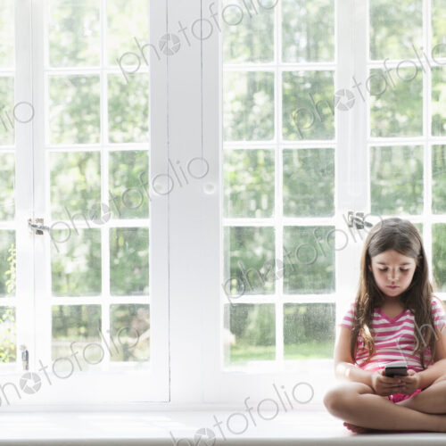 A girl sitting playing, holding a smart phone.