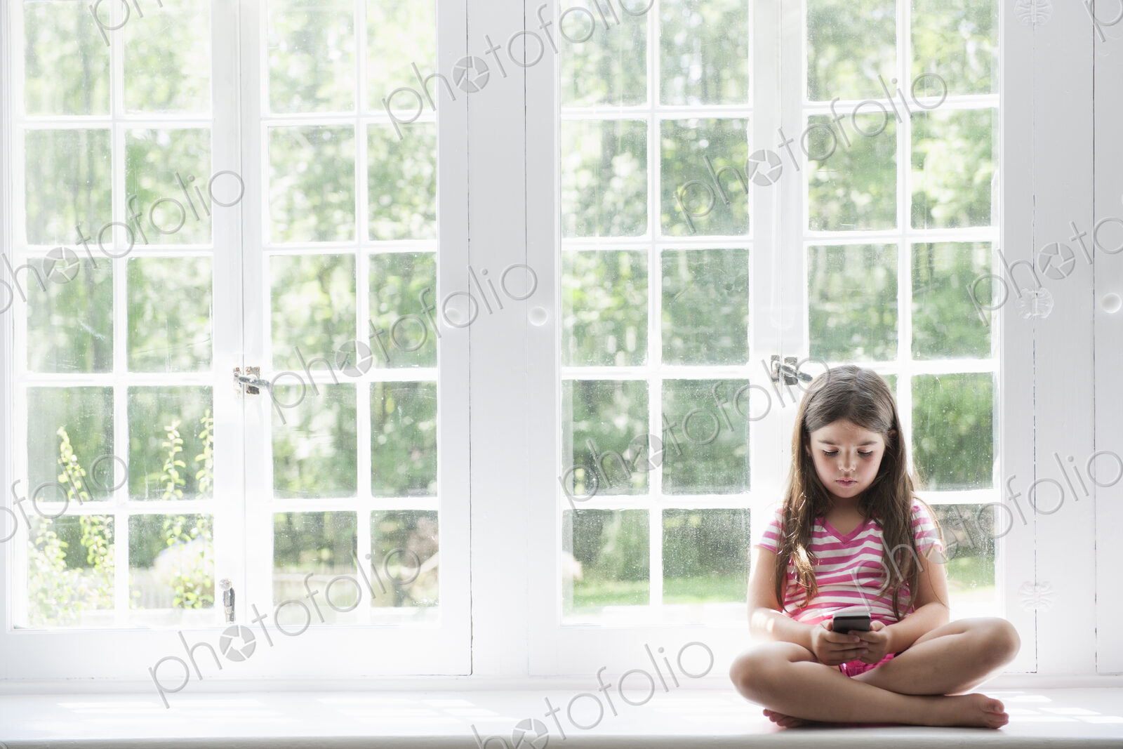 A girl sitting playing, holding a smart phone.