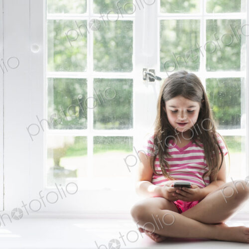 A girl sitting playing, holding a smart phone.