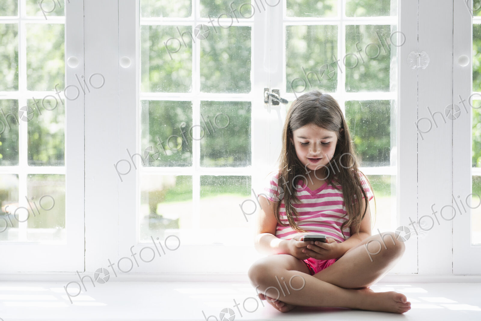 A girl sitting playing, holding a smart phone.