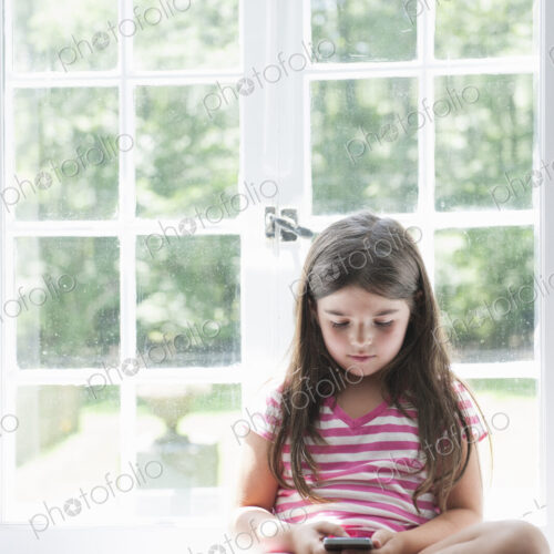 A girl sitting playing, holding a smart phone.