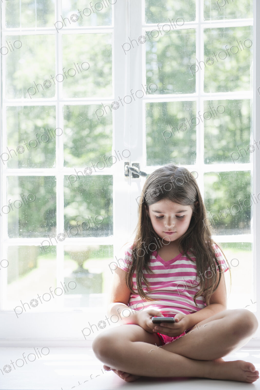 A girl sitting playing, holding a smart phone.