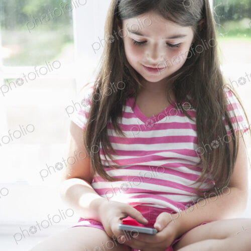 A girl sitting playing, holding a smart phone.