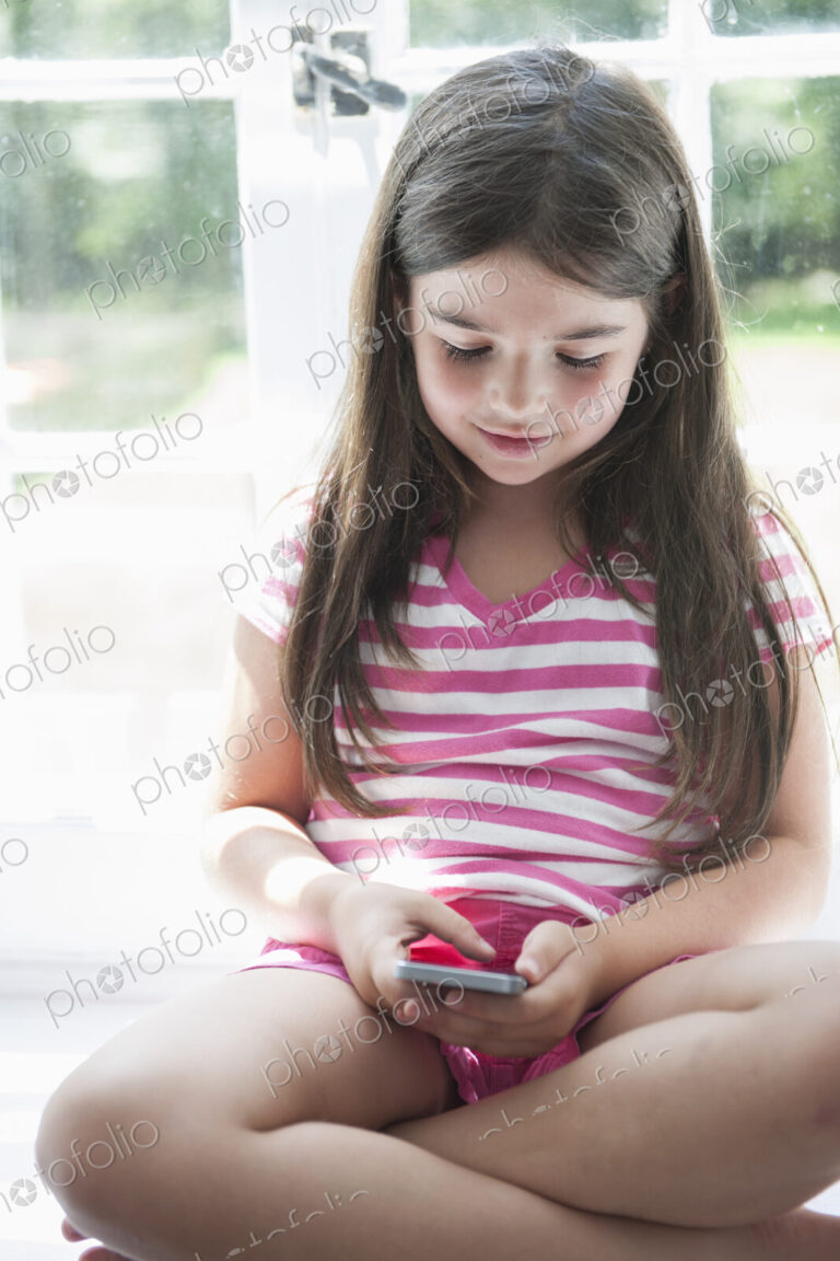 A girl sitting playing, holding a smart phone.