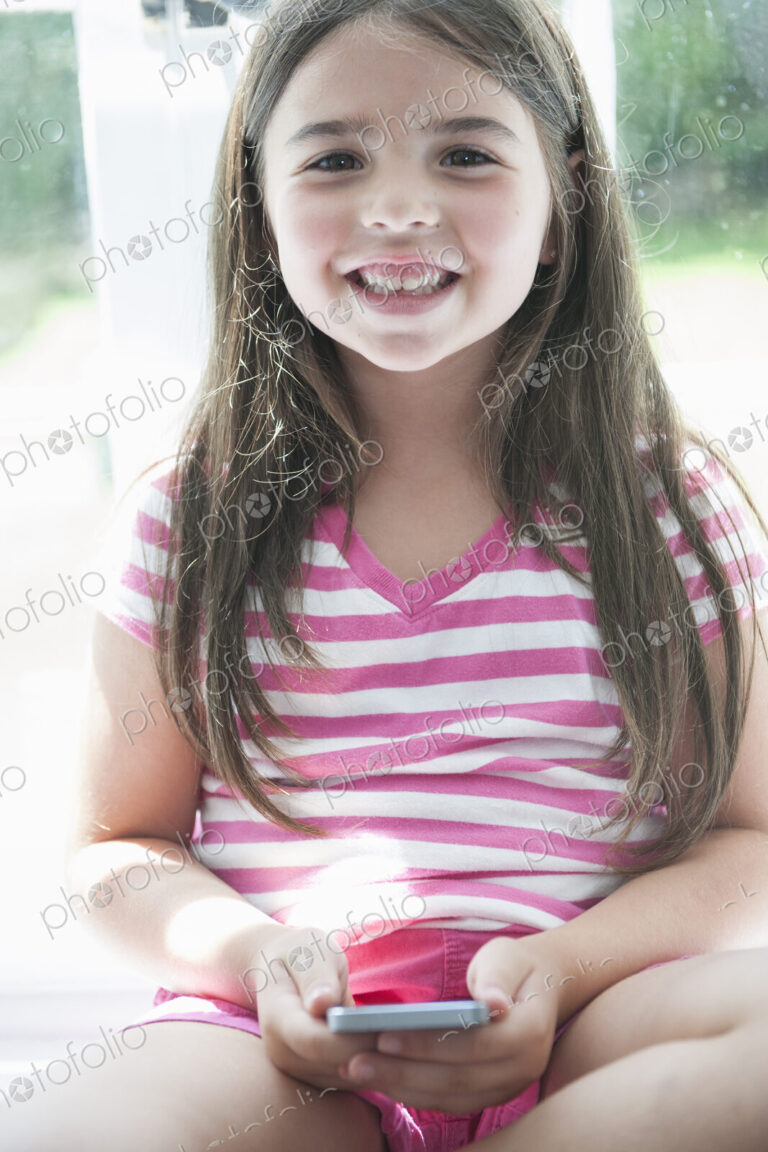 A girl sitting playing, holding a smart phone.