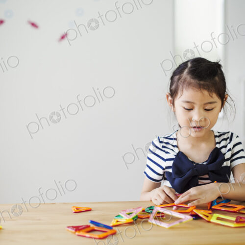 A girl sitting playing with coloured geometric shapes.