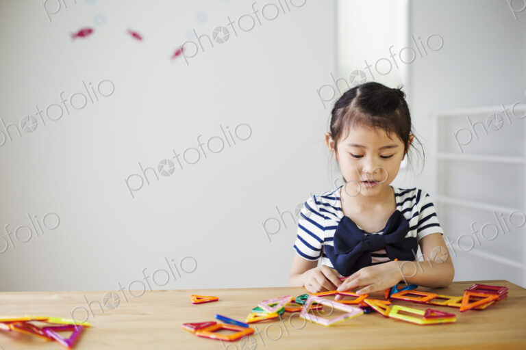 A girl sitting playing with coloured geometric shapes.