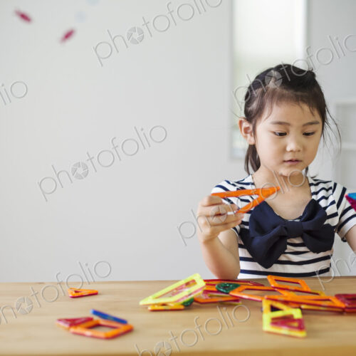 A girl sitting playing with coloured geometric shapes.