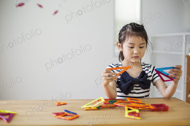 A girl sitting playing with coloured geometric shapes.