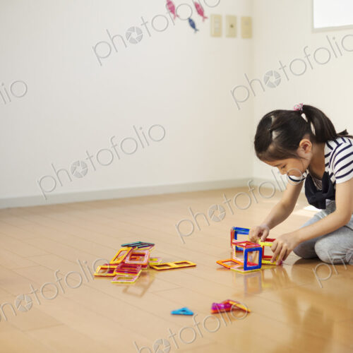 A girl sitting playing with coloured geometric shapes.