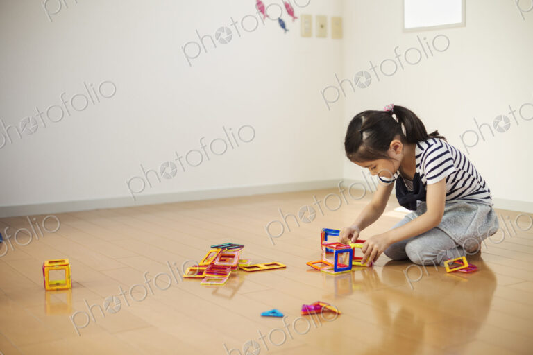 A girl sitting playing with coloured geometric shapes.
