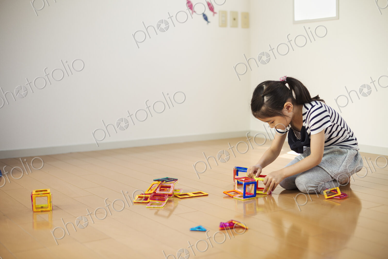 A girl sitting playing with coloured geometric shapes.