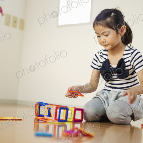 A girl sitting playing with coloured geometric shapes.