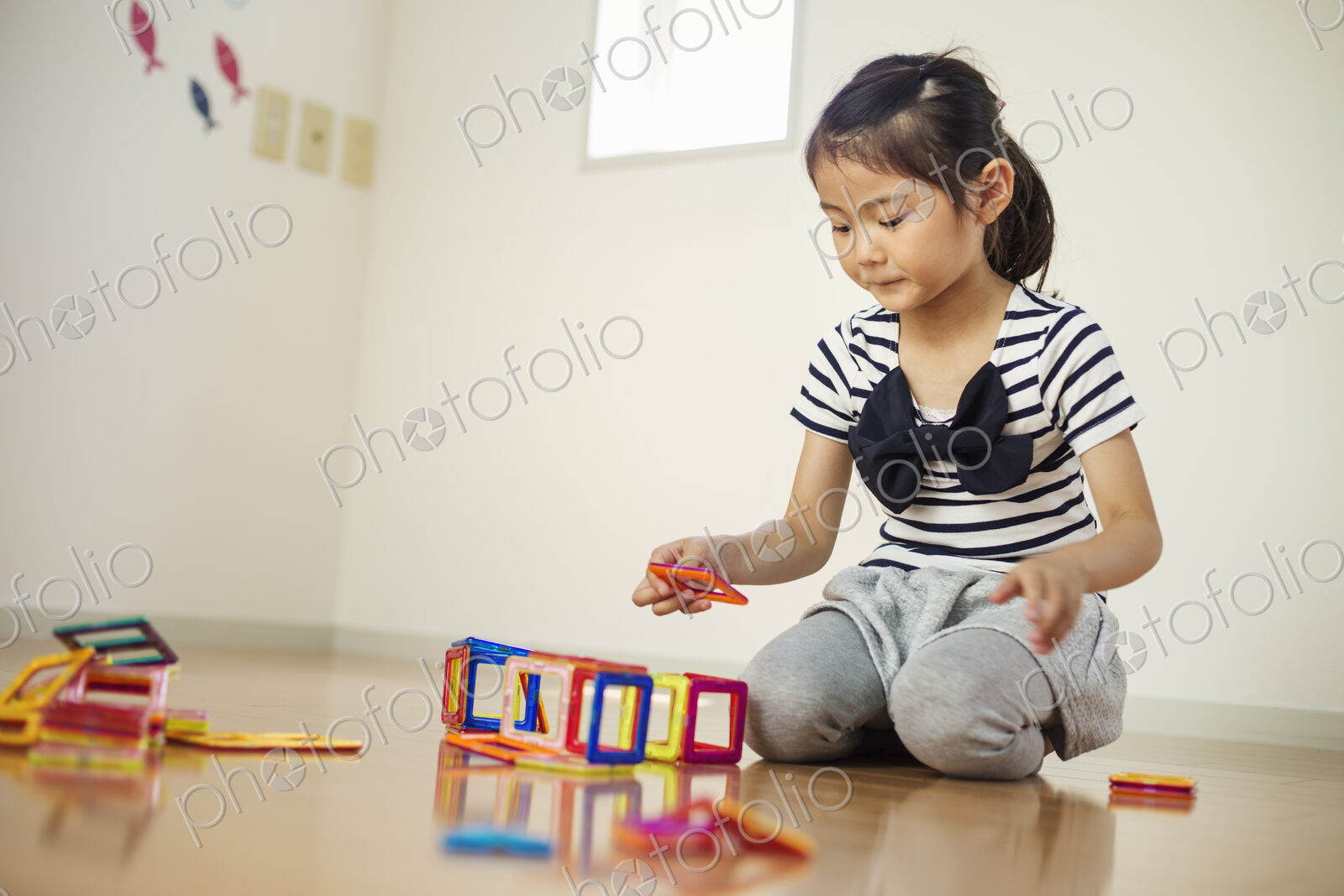 A girl sitting playing with coloured geometric shapes.