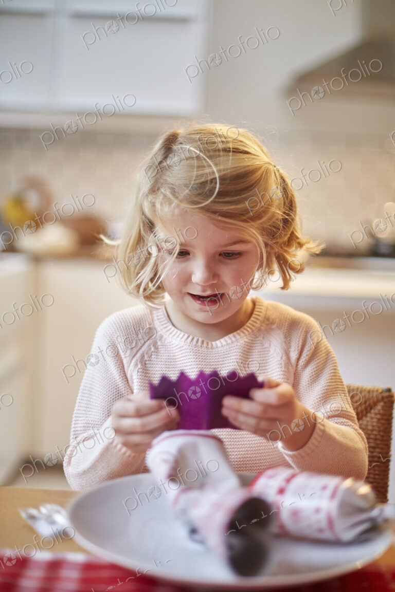 A girl unwrapping a paper hat out of a Christmas cracker.
