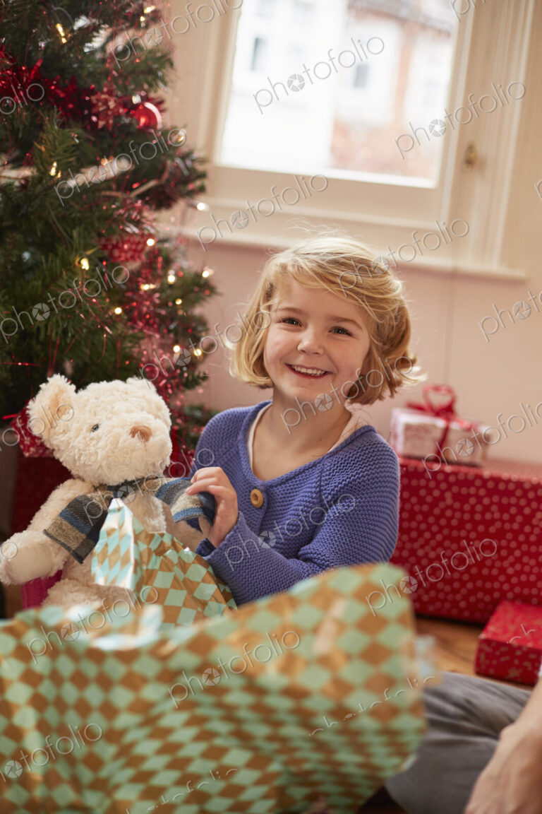 A girl unwrapping a soft toy, a teddy bear, on Christmas Day.