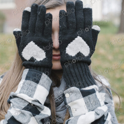 A girl wearing wooly gloves with a heart shaped design, hiding her face.