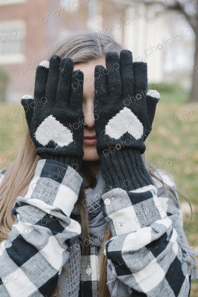 A girl wearing wooly gloves with a heart shaped design, hiding her face.
