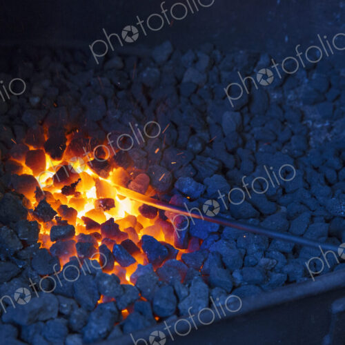 A glowing metal rod in the hot coals in a blacksmith's forge.