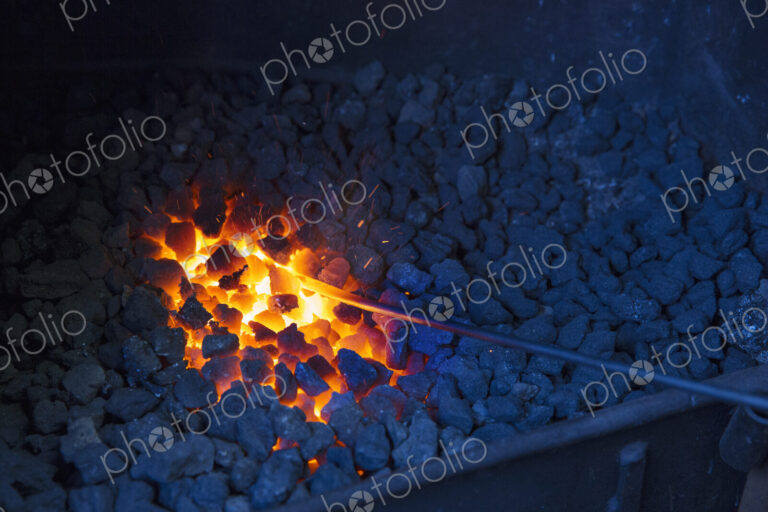 A glowing metal rod in the hot coals in a blacksmith's forge.