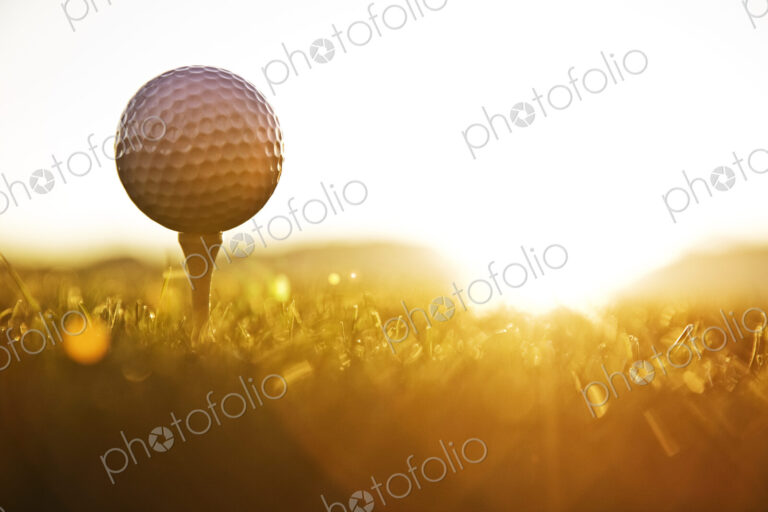 A golf ball on a tee and ready to be hit as the sun comes up.
