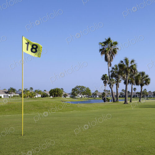 A golf course green with a yellow flag on a post in the hole.