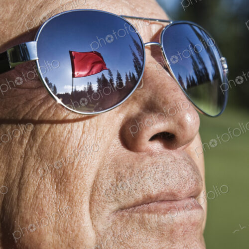 A golf flag on a green reflected in the sunglasses of a senior golfer. A golf flag on a green reflected in the sunglasses of a senior golfer.