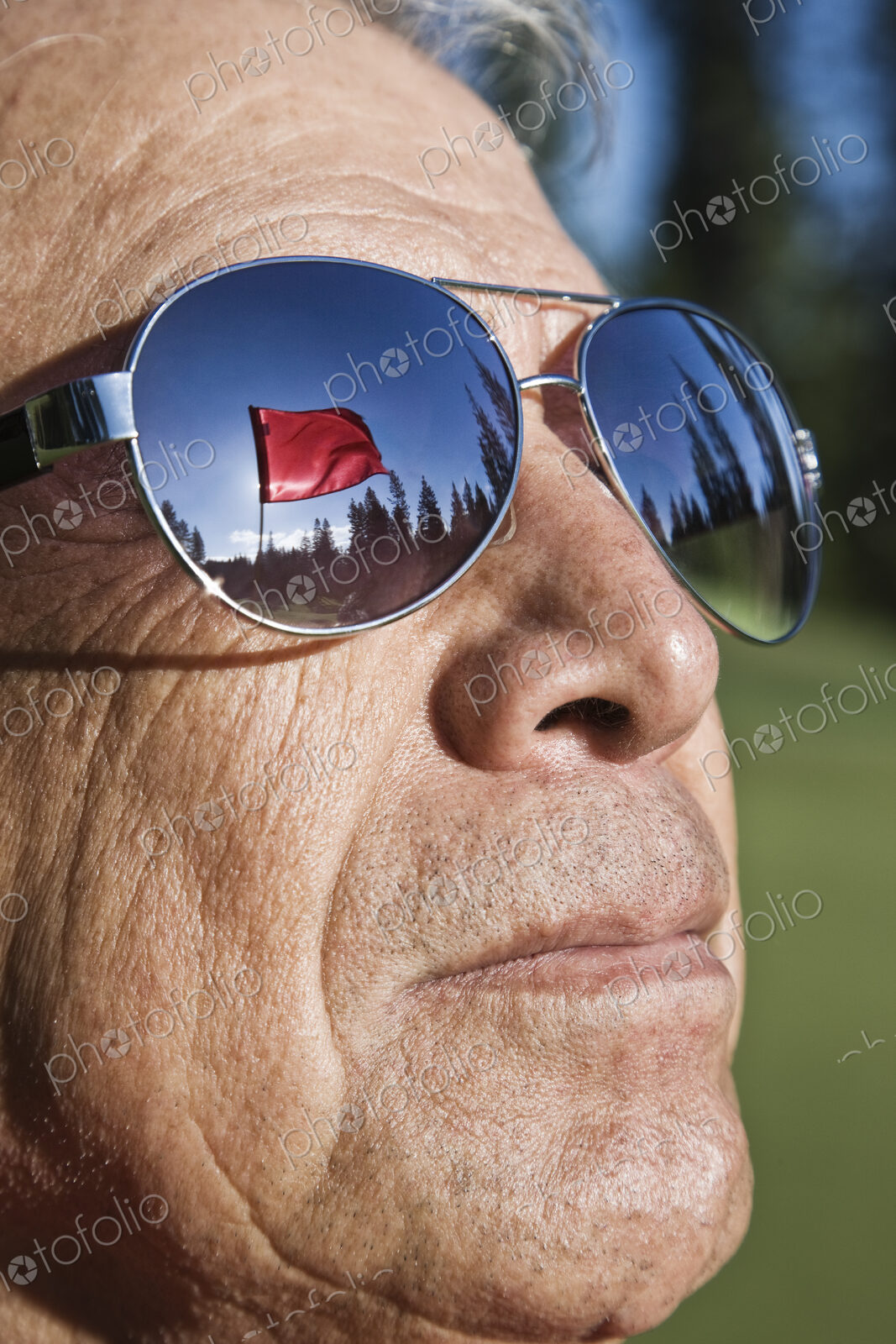 A golf flag on a green reflected in the sunglasses of a senior golfer.