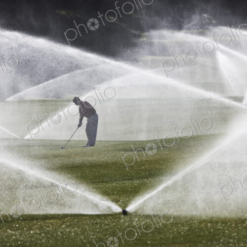 A golfer hitting his second shot on the fairway when the sprinkler system turns on. A golfer hitting his second shot on the fairway when the sprinkler system turns on.