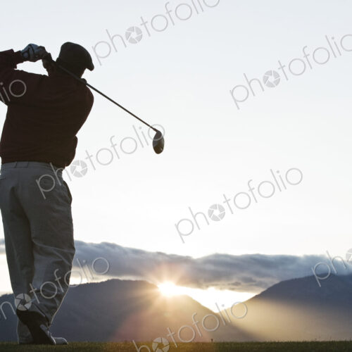 A golfer teeing off at sunrise. A golfer teeing off at sunrise.