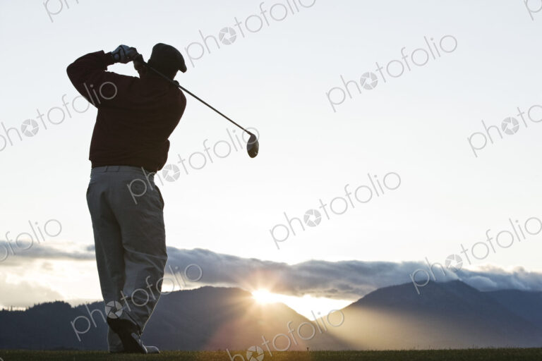 A golfer teeing off at sunrise.