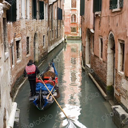 A gondola boat gliding down a small narrow waterway, between historic houses in the…