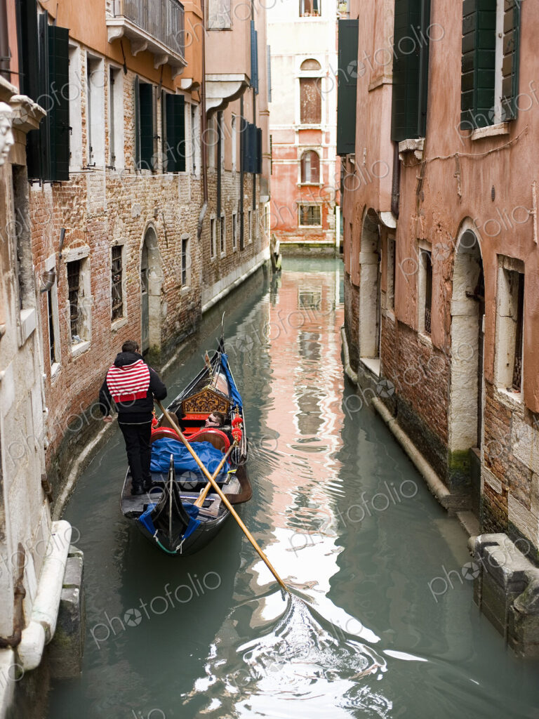 A gondola boat gliding down a small narrow waterway, between historic houses in the…