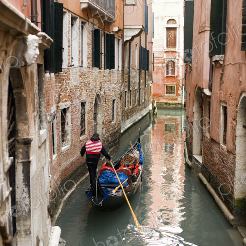 A gondola boat gliding down a small narrow waterway, between historic houses in the…