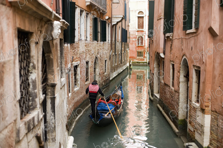 A gondola boat gliding down a small narrow waterway, between historic houses in the…